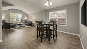 A spacious living area with a dining table, chairs, and a chandelier. There are two windows with blinds, a fireplace, and a flat-screen TV mounted on the wall. - Superb 4-bedroom house with AC in Fort Worth (Fort Worth)