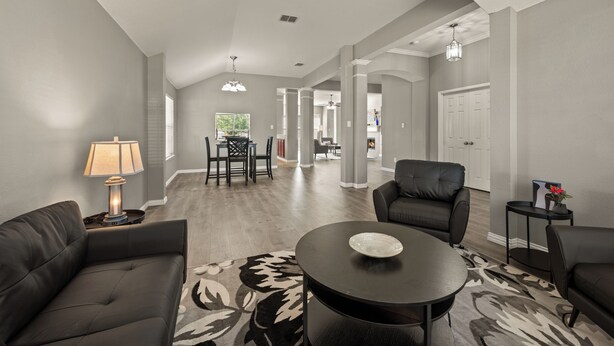 A spacious living room with a dark leather sofa, a round coffee table, and a patterned rug. There is a dining area with a chandelier and a view of the outdoors. - Superb 4-bedroom house with AC in Fort Worth (Fort Worth)