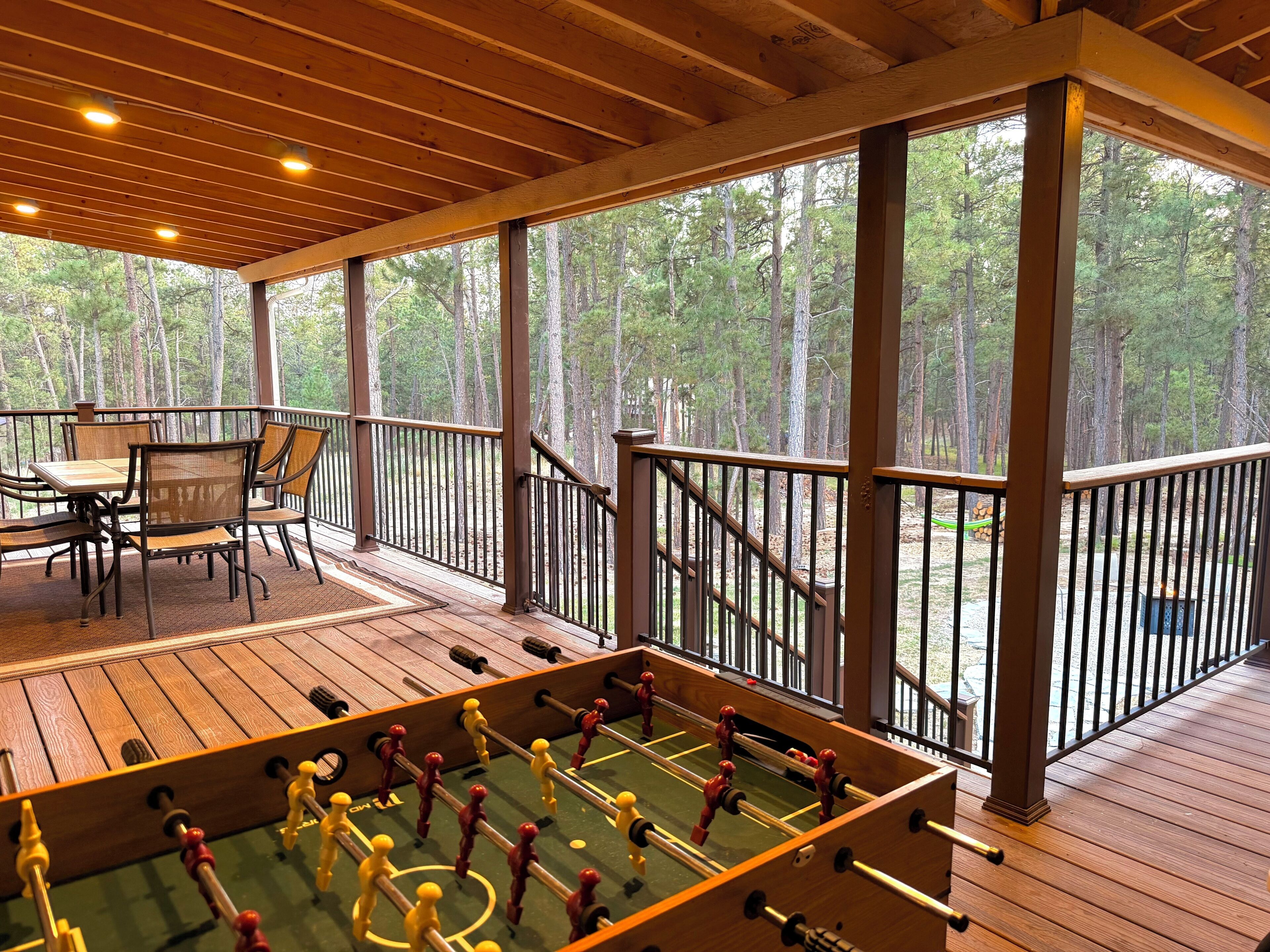 Une terrasse en bois avec un baby-foot, des chaises et une table offrant une vue sur la forêt.