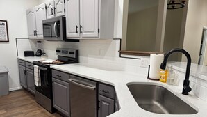 Una cocina moderna con armarios blancos, electrodomésticos de acero inoxidable y un lavamanos grande.