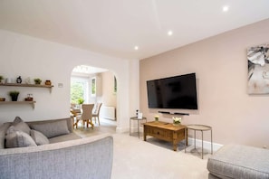 Un salon moderne avec un téléviseur à écran plat, un canapé, une table basse et un coin repas à l’arrière-plan.