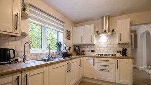 Eine Küche mit weißen Schränken, einem Gasherd, einer Kaffeemaschine und einem Fenster mit Jalousien.
