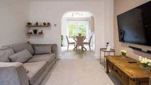Ein Wohnzimmer mit einer Couch, einem Fernseher, einem Holztisch und einem Essbereich mit Tisch und Stühlen.