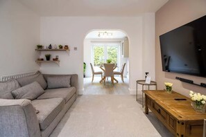 A living room with a sofa, a TV, a wooden coffee table, and a dining area with a table and chairs.