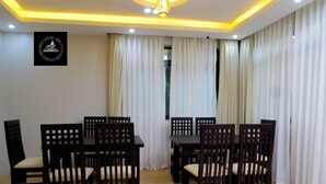 A dining area with wooden tables and chairs, a ceiling with recessed lighting, and a logo on the wall. - Residence Six Sigma (Entebbe)