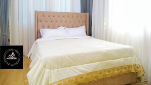 A neatly made bed with a tufted headboard, white linens, and a gold trim at the foot of the bed. - Residence Six Sigma (Entebbe)