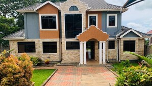 A two-story house with a central entrance, large windows, and a landscaped front yard. - Residence Six Sigma (Entebbe)