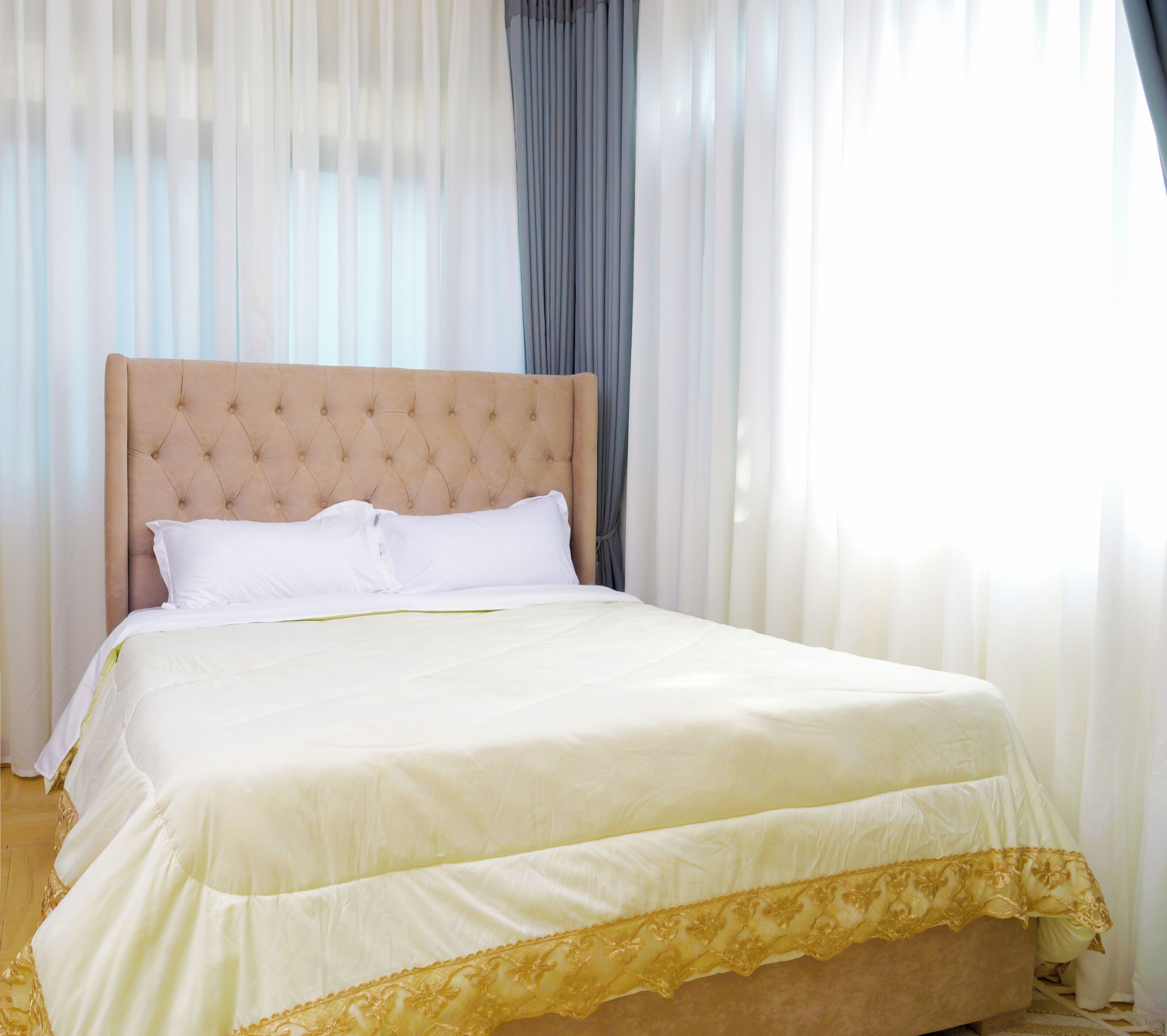 A neatly made bed with a tufted headboard, white linens, and a gold trim at the foot of the bed.