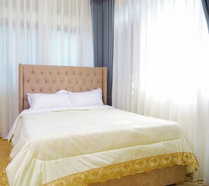 A neatly made bed with a tufted headboard, white linens, and a gold trim at the foot of the bed. - Residence Six Sigma (Entebbe)