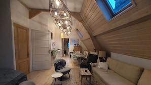 A cozy attic room with a sloped ceiling, wooden beams, a sofa, armchairs, a small table, and a hanging light fixture. - Historic townhouse with 5 bedrooms In Holland's oldest city center, airco (Dordrecht)