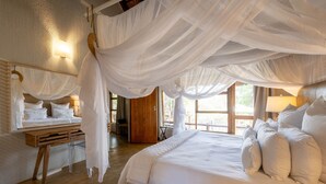 A bedroom with a large bed, white bedding, a wooden desk, and a window with a view. - Karongwe - Noka House (Hoedspruit)