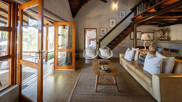 A spacious living area with a wooden ceiling, a staircase, and a view through large glass doors to an outdoor deck. - Karongwe - Noka House (Hoedspruit)