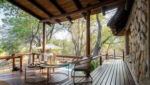 A wooden deck with a table and chairs, surrounded by trees. - Karongwe - Noka House (Hoedspruit)