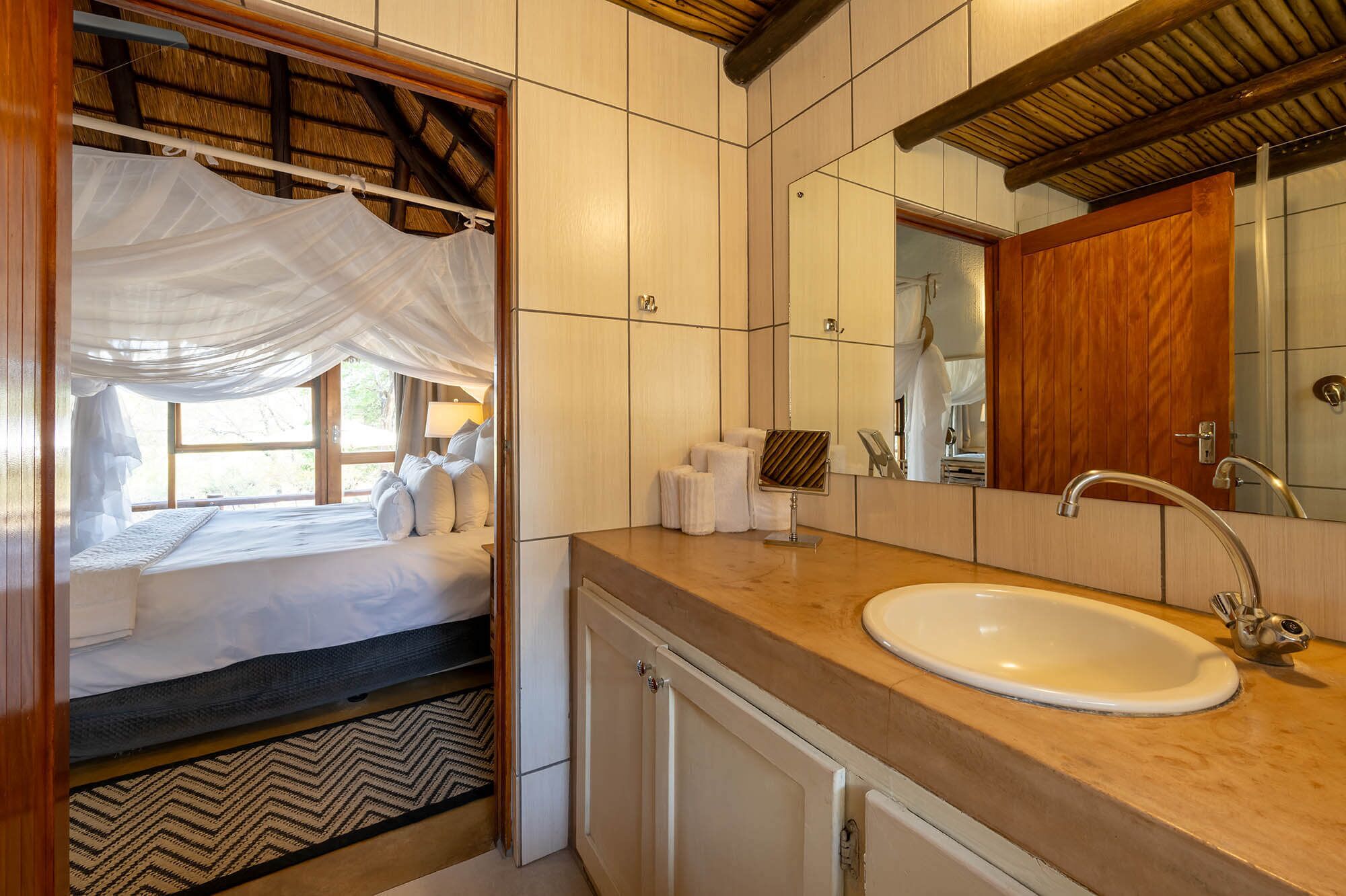 A bedroom with a bed, a bedside table, a mirror, and a window with a view.
