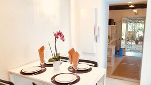 Comedor con una mesa blanca dispuesta para cuatro personas, sillas negras y una orquídea en maceta.