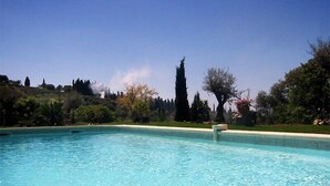 Piscina azul cristalina con vistas a un jardín ajardinado y colinas lejanas.