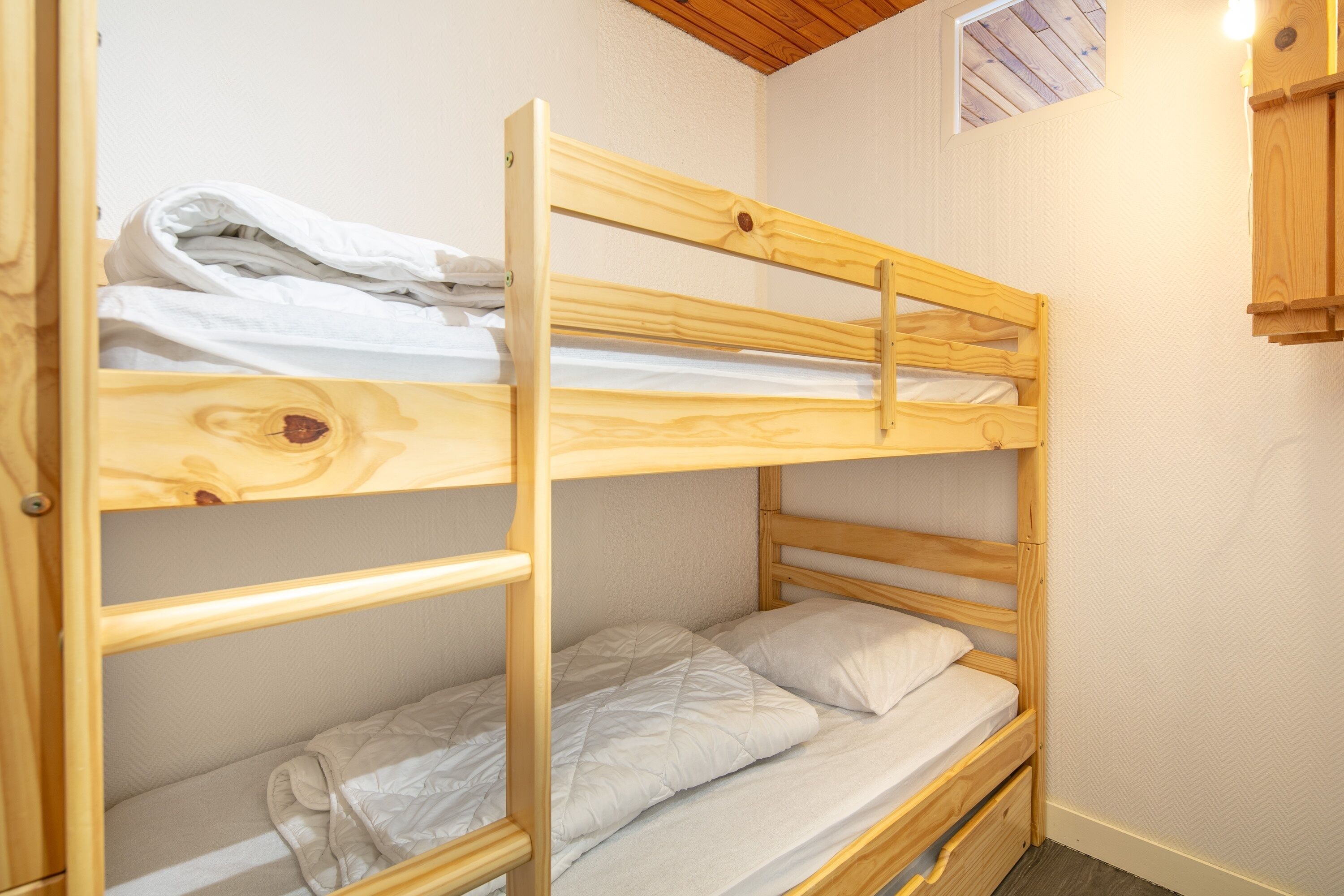 A bunk bed with a wooden frame, a lower shelf, and a small window above the upper bunk.
