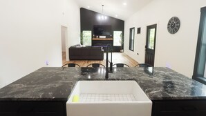 Eine moderne Küche mit Marmorarbeitsplatte, integriertem Spülbecken und einem Essbereich mit dunklem Sofa und Stühlen.