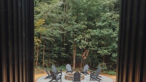Ein kreisförmiger Sitzbereich mit Adirondack-Stühlen um eine zentrale Feuerstelle, umgeben von einem Kiesweg und einem bewaldeten Hintergrund.