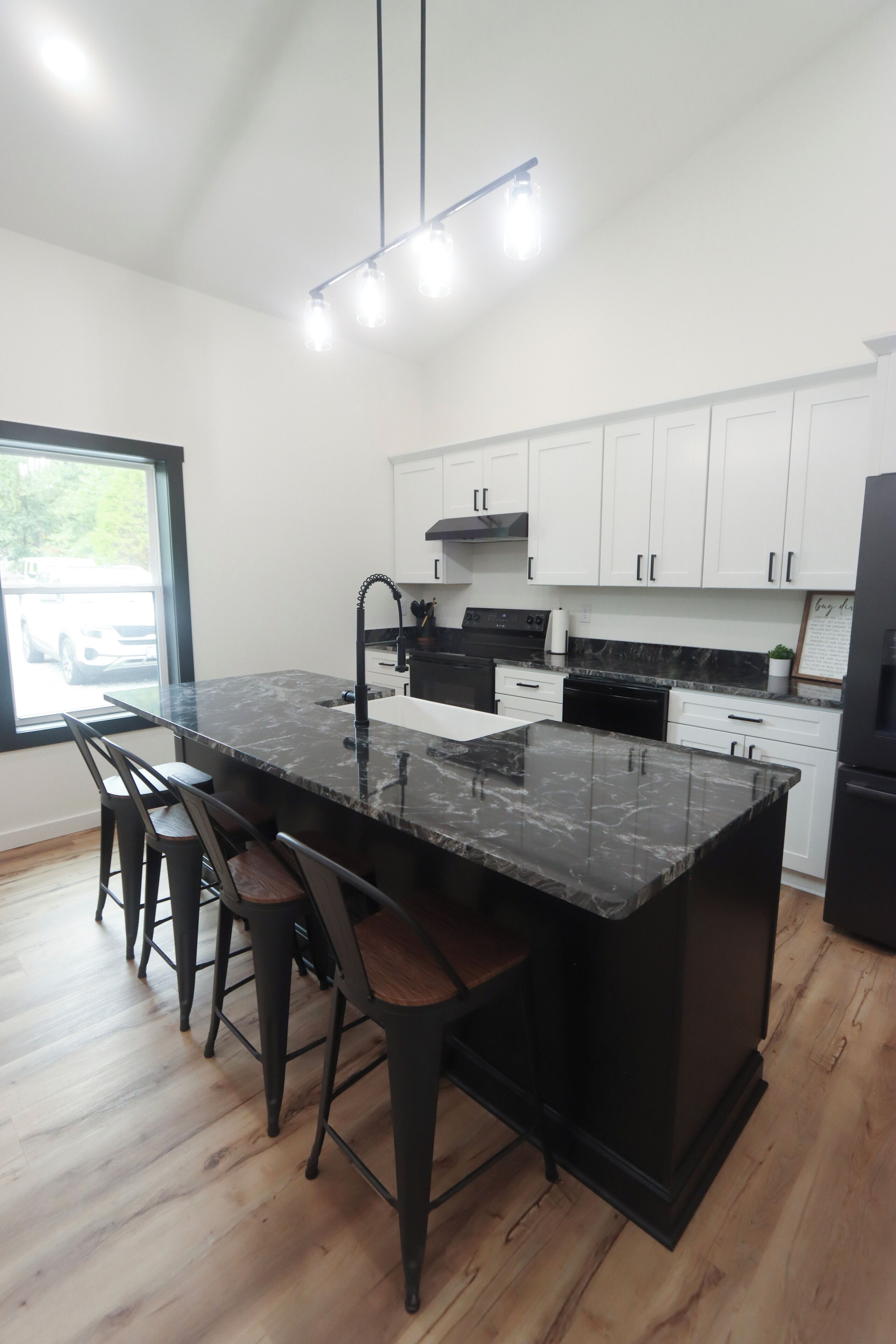 A modern kitchen with a marble island, bar stools, white cabinets, and a black refrigerator.