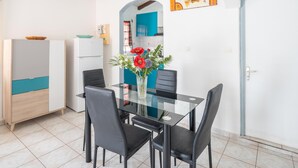 Un coin repas avec une table en verre et des chaises noires, un vase rempli de fleurs et, au fond, une cuisine.