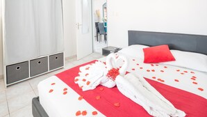 Une chambre d’hôtel avec un lit, une couvre-lit rouge et blanche, un oreiller rouge et une serviette décorée de pétales de rose.