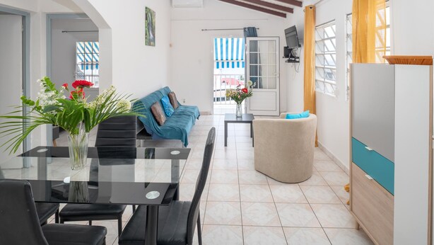 Un salon moderne avec une table à manger en verre, un canapé bleu et un pouf beige.