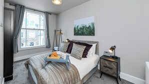 Une chambre à coucher avec un lit, une table de chevet, une lampe et une fenêtre avec des rideaux.