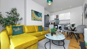Un salon moderne avec un canapé jaune, une table basse ronde et un coin repas avec des chaises grises.