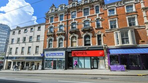 Une vue de rue avec une rangée de bâtiments, dont un magasin portant l’enseigne « Phone Garage » et un salon de coiffure.