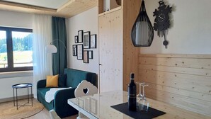 Een moderne woonkamer met een groene bank, een klein wit tafeltje en een houten kast. Er hangen ingelijste foto's aan de muur en er staat een bijzondere klok.
