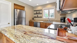 Una cocina con encimeras de granito, electrodomésticos de acero inoxidable, armarios de madera y un ventanal que proporciona luz natural.