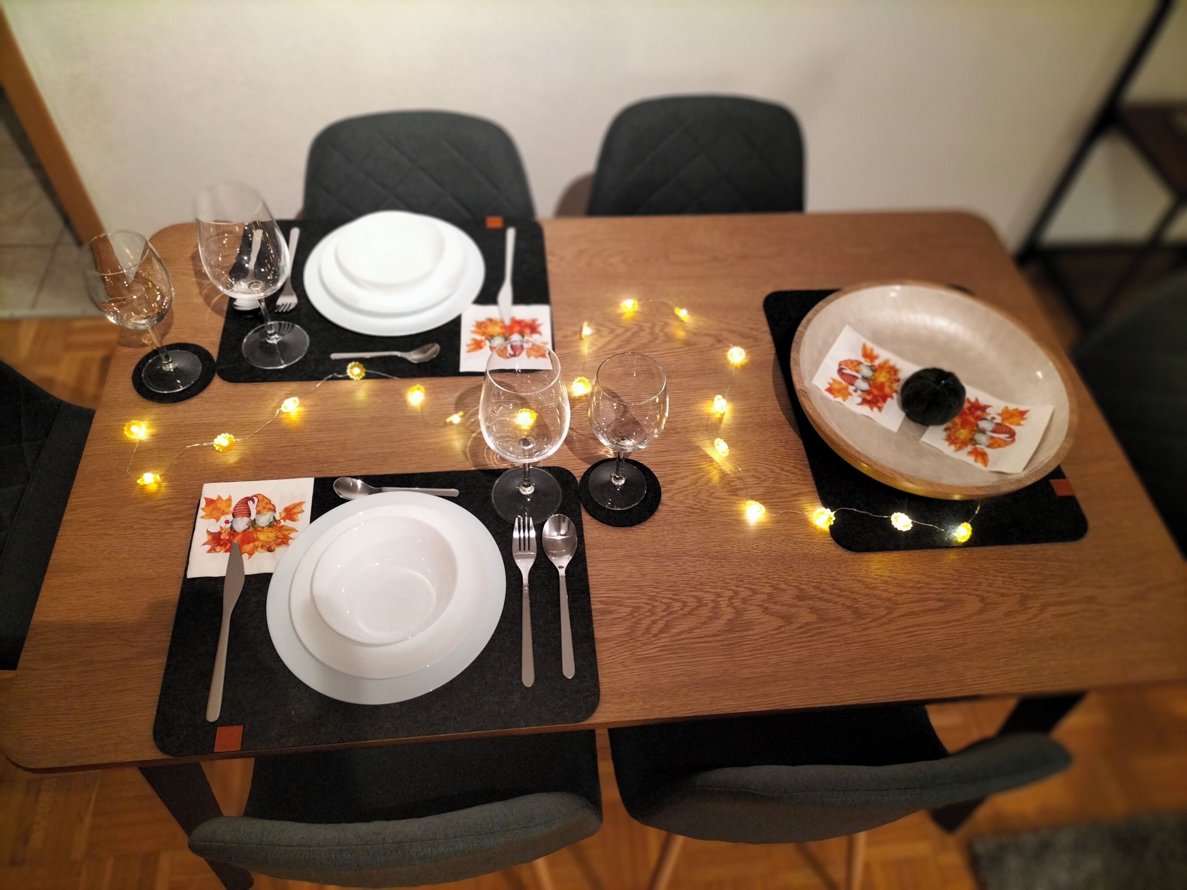 Une table à manger dressée avec des assiettes, des couverts et des verres à vin, le tout illuminé par des guirlandes lumineuses.