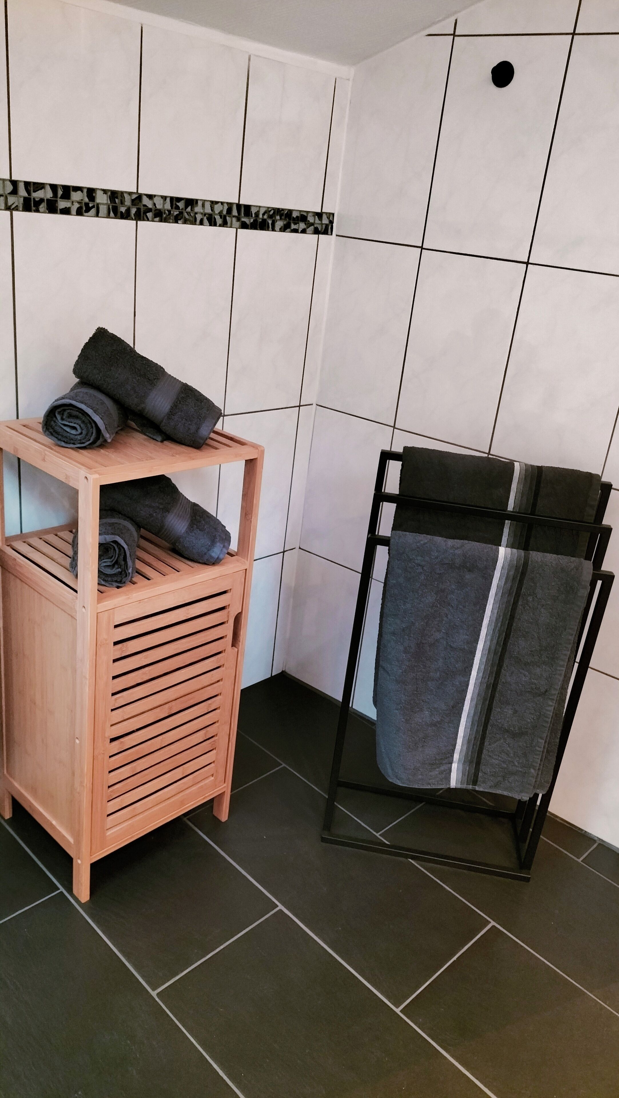 A bathroom with a wooden towel rack, a towel shelf, and a tiled floor.