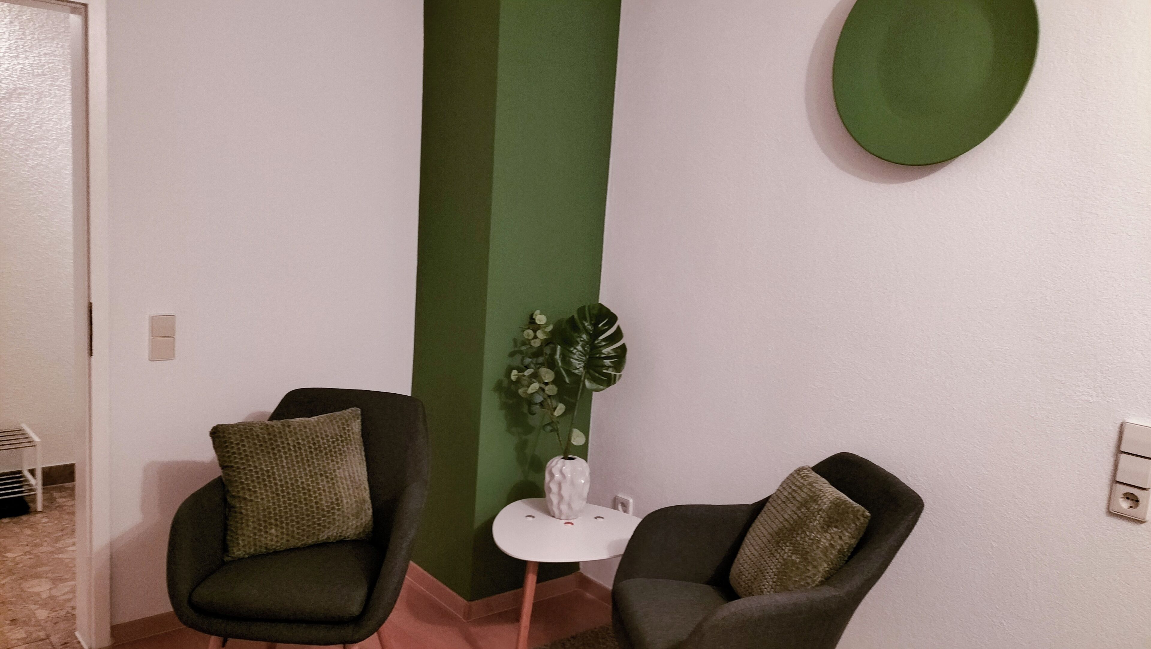 Una habitación con dos sillones, una mesita pequeña y una pared de acento verde.