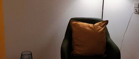 A room with a framed artwork, a lamp, a chair, a small table, and a floor lamp.