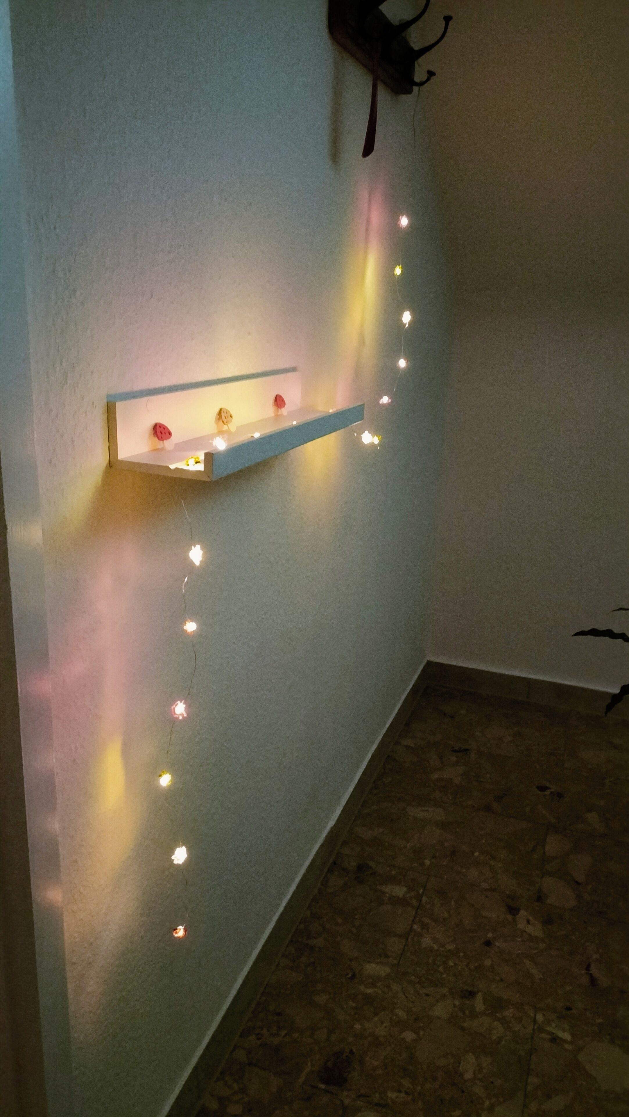 Una esquina de una habitación con una pared blanca, una estantería con luces decorativas y una cabeza de ciervo montada en la pared.