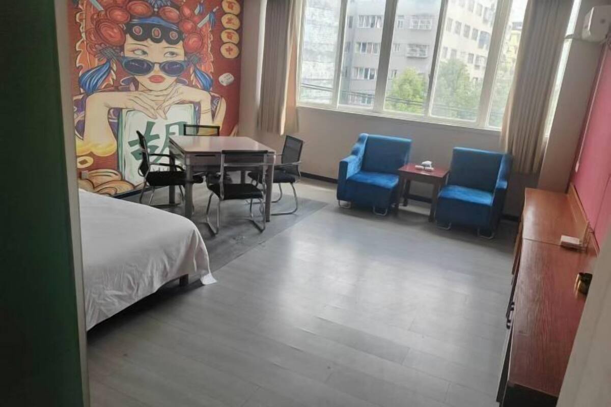 A hotel room with a bed, a desk with chairs, a small table, and two blue armchairs.