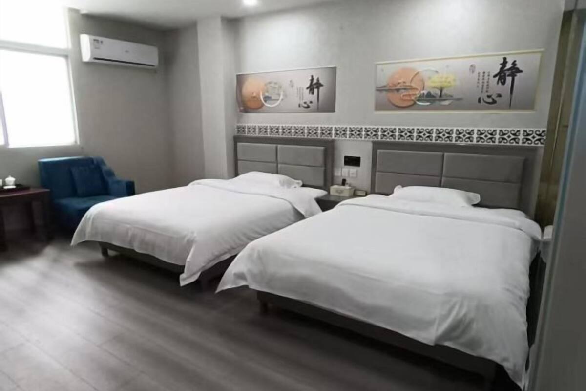 A hotel room with two beds, a blue chair, and artwork on the wall.