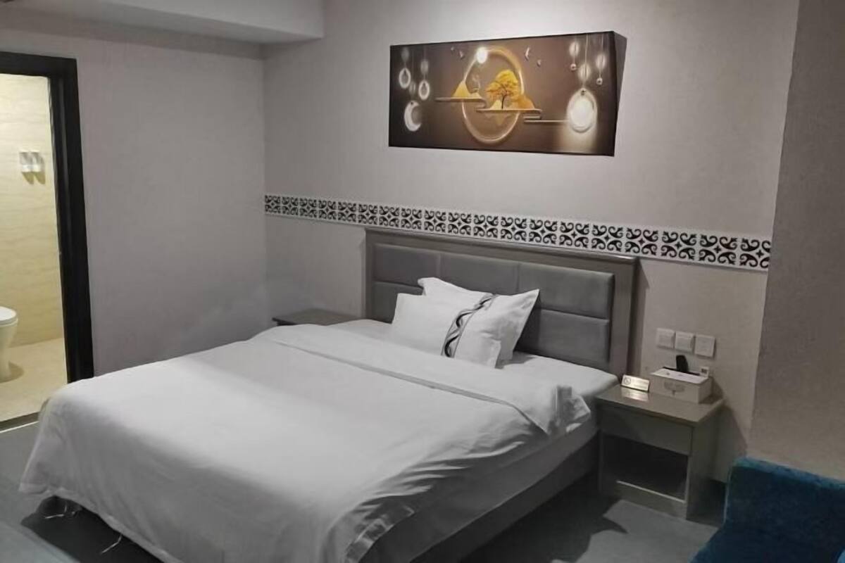 A modern hotel room with a bed, a nightstand, a wall-mounted artwork, and a patterned border above the bed.