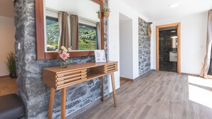 Un espace d’accueil avec un mur en pierre, une console en bois et un miroir qui reflète un paysage pittoresque.