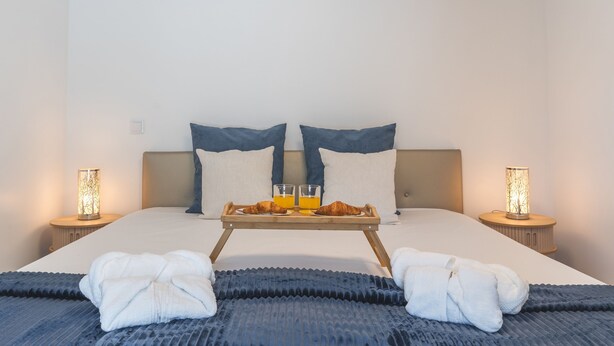 Un lit bien fait avec deux oreillers, un plateau avec des croissants et du jus d’orange, et deux lampes de chevet.