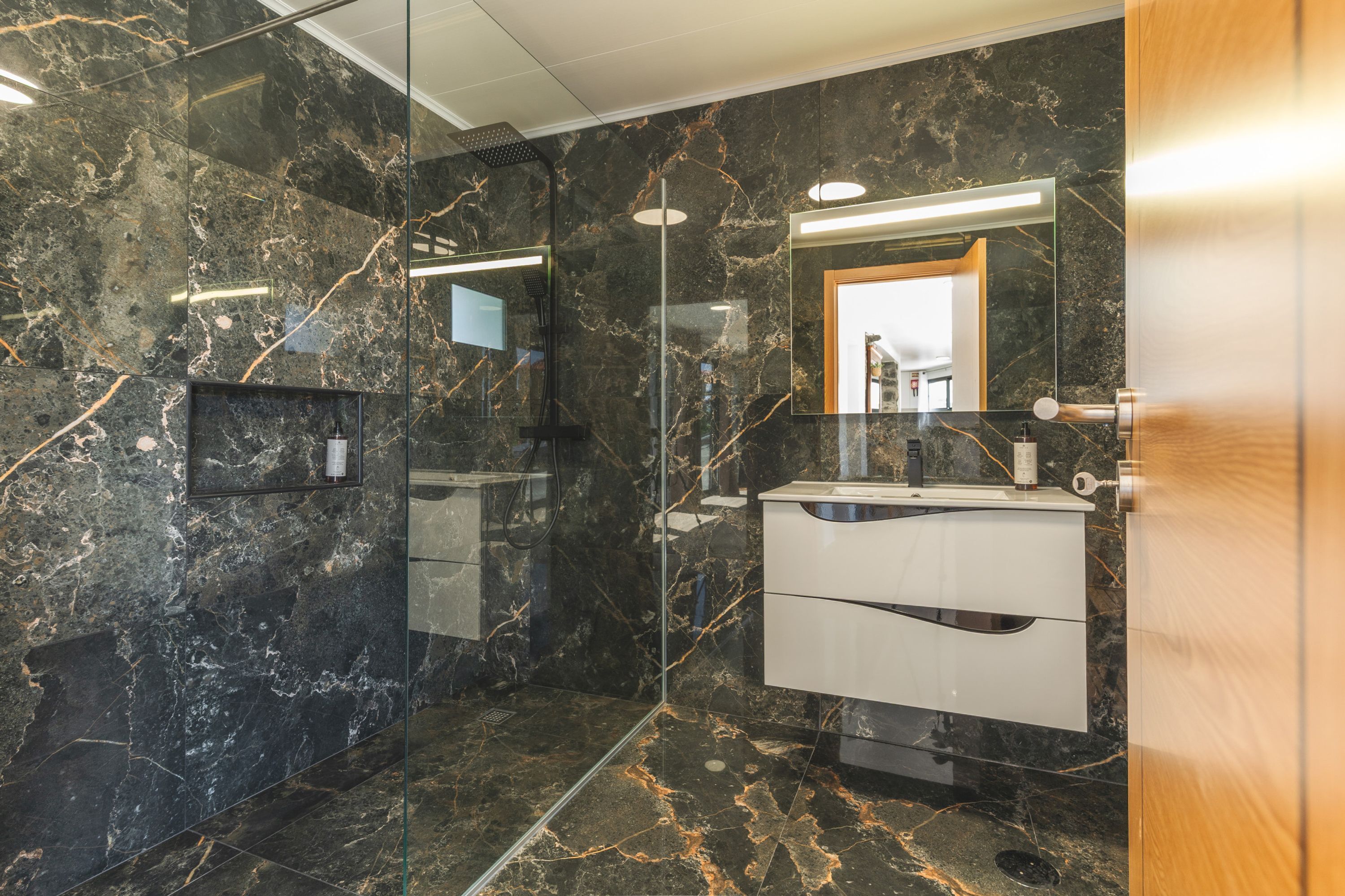 A modern bathroom with a glass-enclosed shower, marble walls, and a vanity with a mirror.