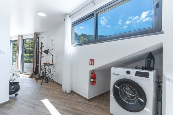 Un espace buanderie comprenant un lave-linge, un extincteur, une table avec une lampe et une vue sur l’extérieur par une fenêtre.