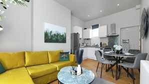 Una sala de estar moderna con un sofá amarillo, una mesa de centro redonda de mármol y una zona de comedor con sillas grises.