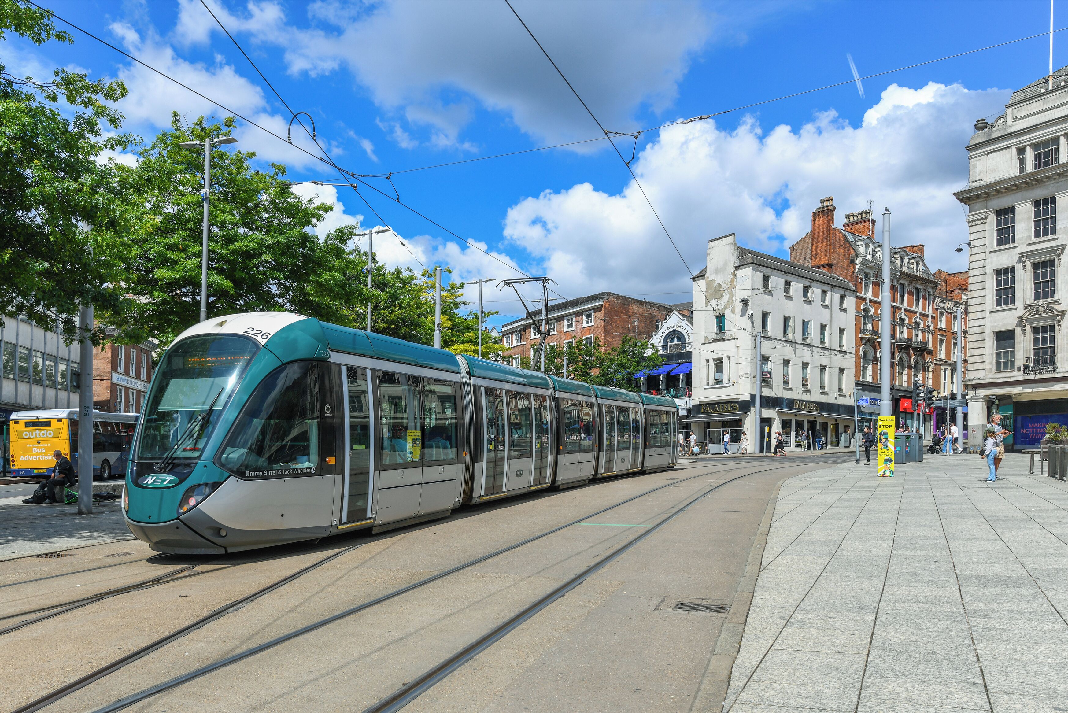 A modern tram on tracks in an urban setting with historic buildings in the background.