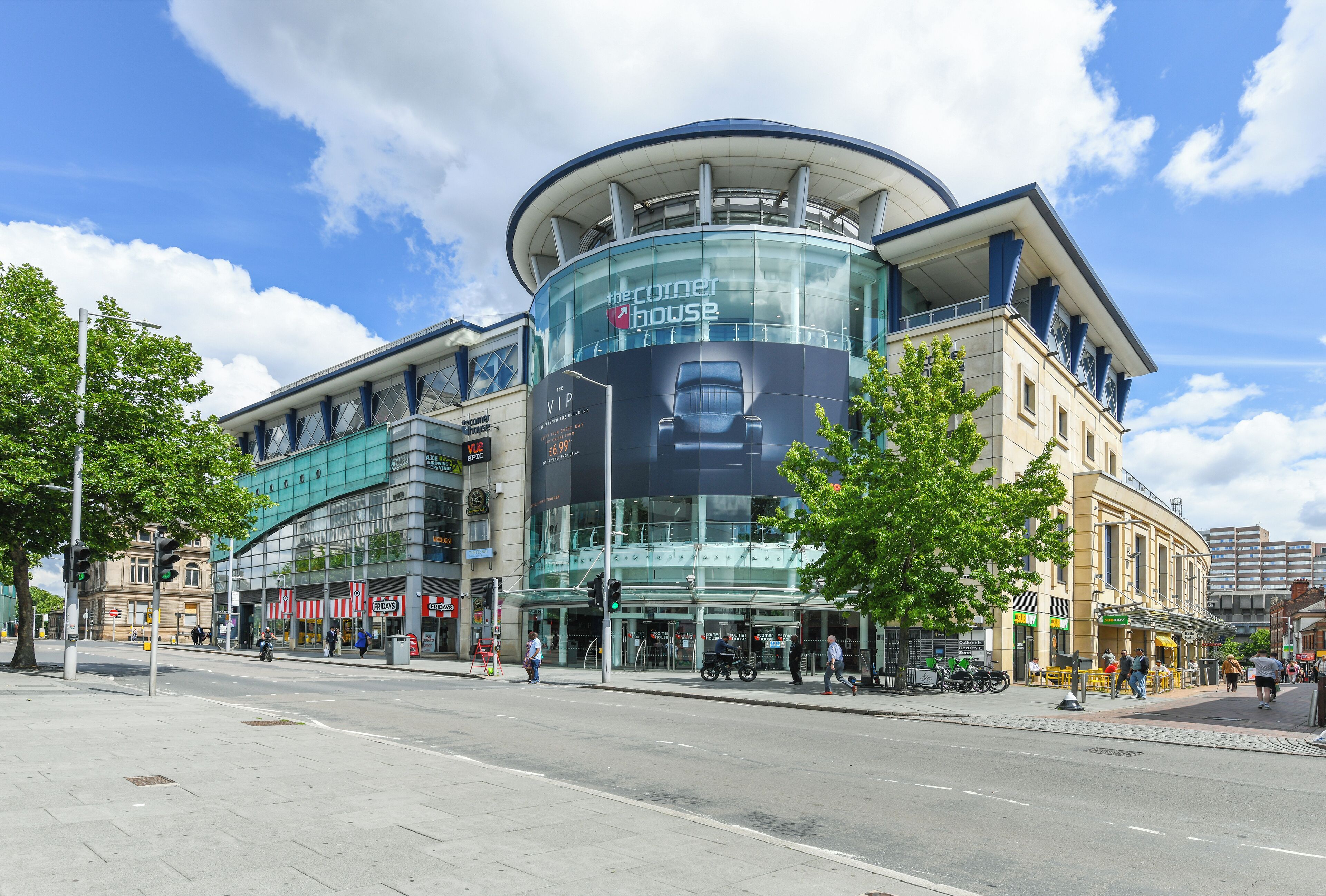 A modern building with a curved glass facade, a prominent advertisement for a hotel, and a pedestrian walkway.