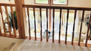 A high-ceilinged room with wooden beams, a balcony with a railing, and a view of greenery outside. - Serene Waterfront 3-BR house with Loft, 1 mile walk to Charlestown beach (Charlestown)