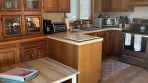 A kitchen with wooden cabinets, a central island, a microwave, a stove, and a dining table. - Serene Waterfront 3-BR house with Loft, 1 mile walk to Charlestown beach (Charlestown)