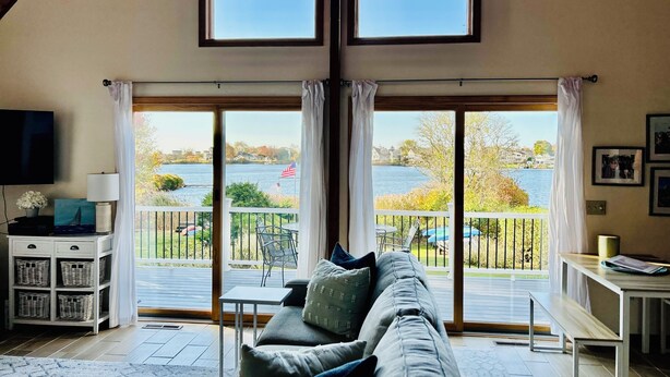 A living room with a large window overlooking a lake, a sofa, a TV, and a small table. - Serene Waterfront 3-BR house with Loft, 1 mile walk to Charlestown beach (Charlestown)